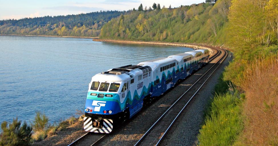 Sounder Everett train moving on tracks surrounded by trees and a lake.