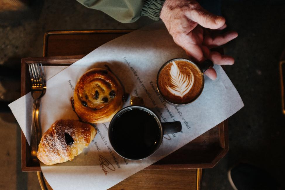 Pastries and mugs with black coffee and a latte on a tray