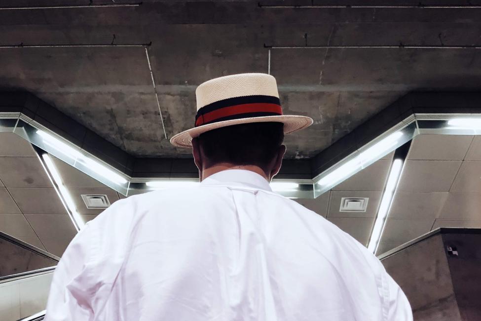 The back of a person's head as they sport a cool fedora while going up an escalator in a 1 Line station