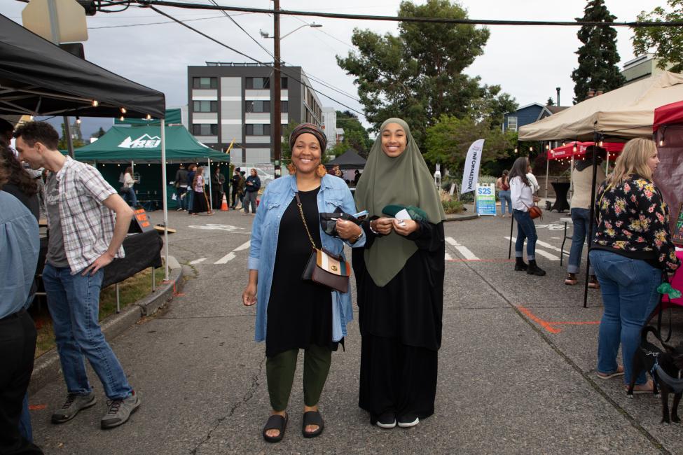 Two night market attendees stand in the street and smile at the camera