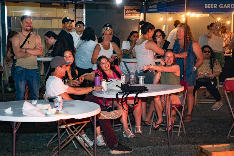 A group of night market attendees smile and look on as a performance happens