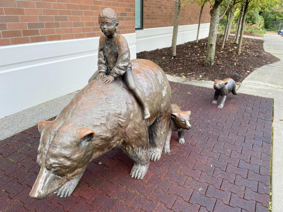 A bronze statue of a child riding on the back of a bear, with two baby bears trailing behind