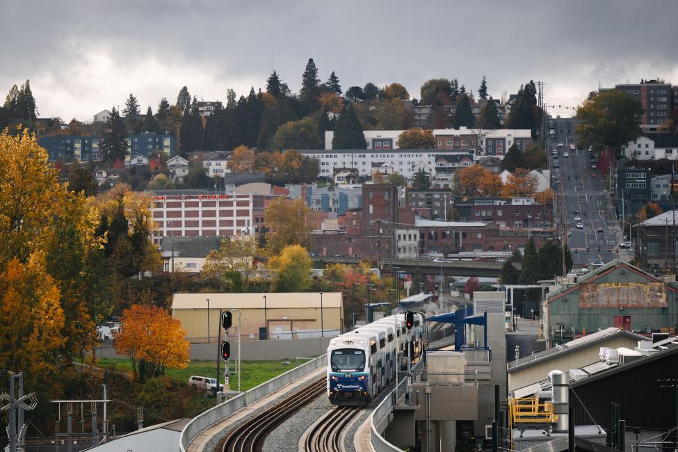 A Sounder train in Tacoma, with houses on a hill in the background 