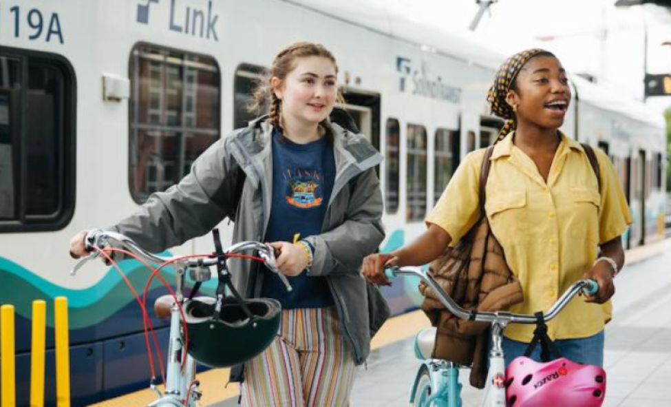 Two passengers stand on a platform with their bikes outside a Link light rail train.