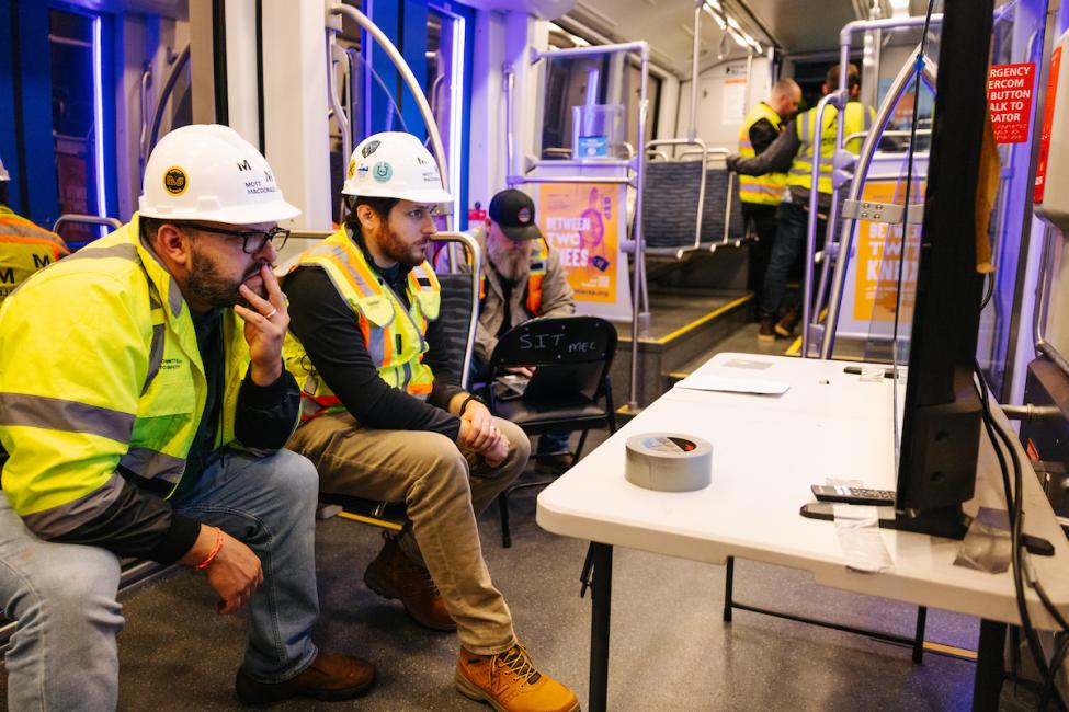 Workers sit in front of a screen as they test wires that power the trains