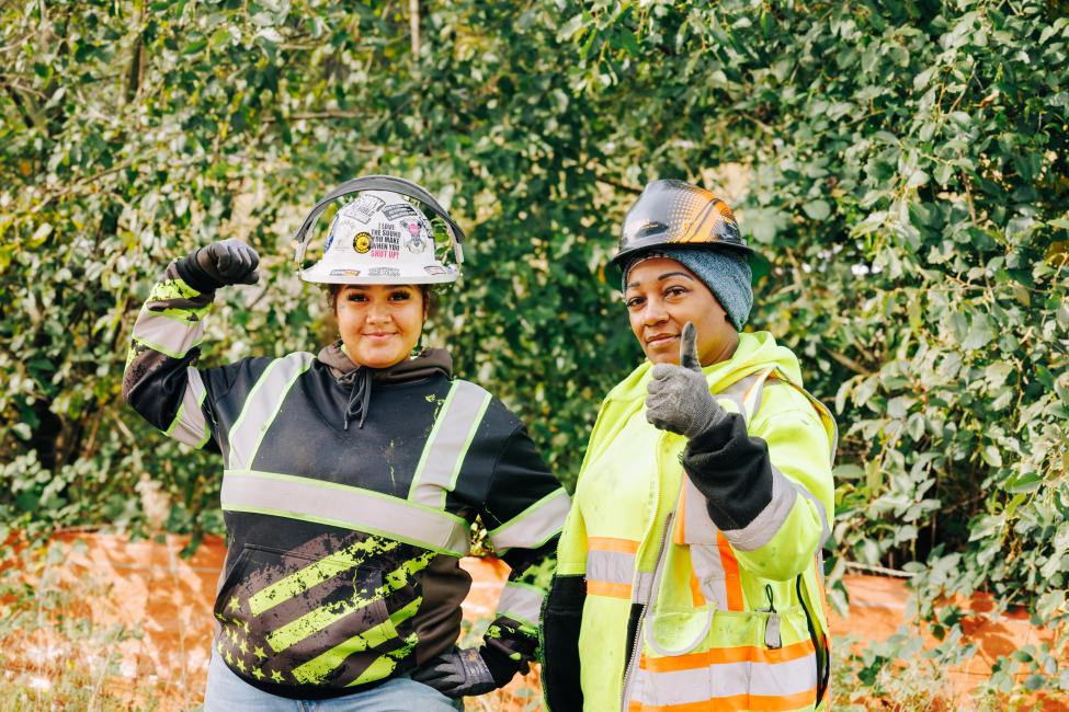 Cicelia Thompson and Katherine Fair flex and give the thumbs up on a construction site