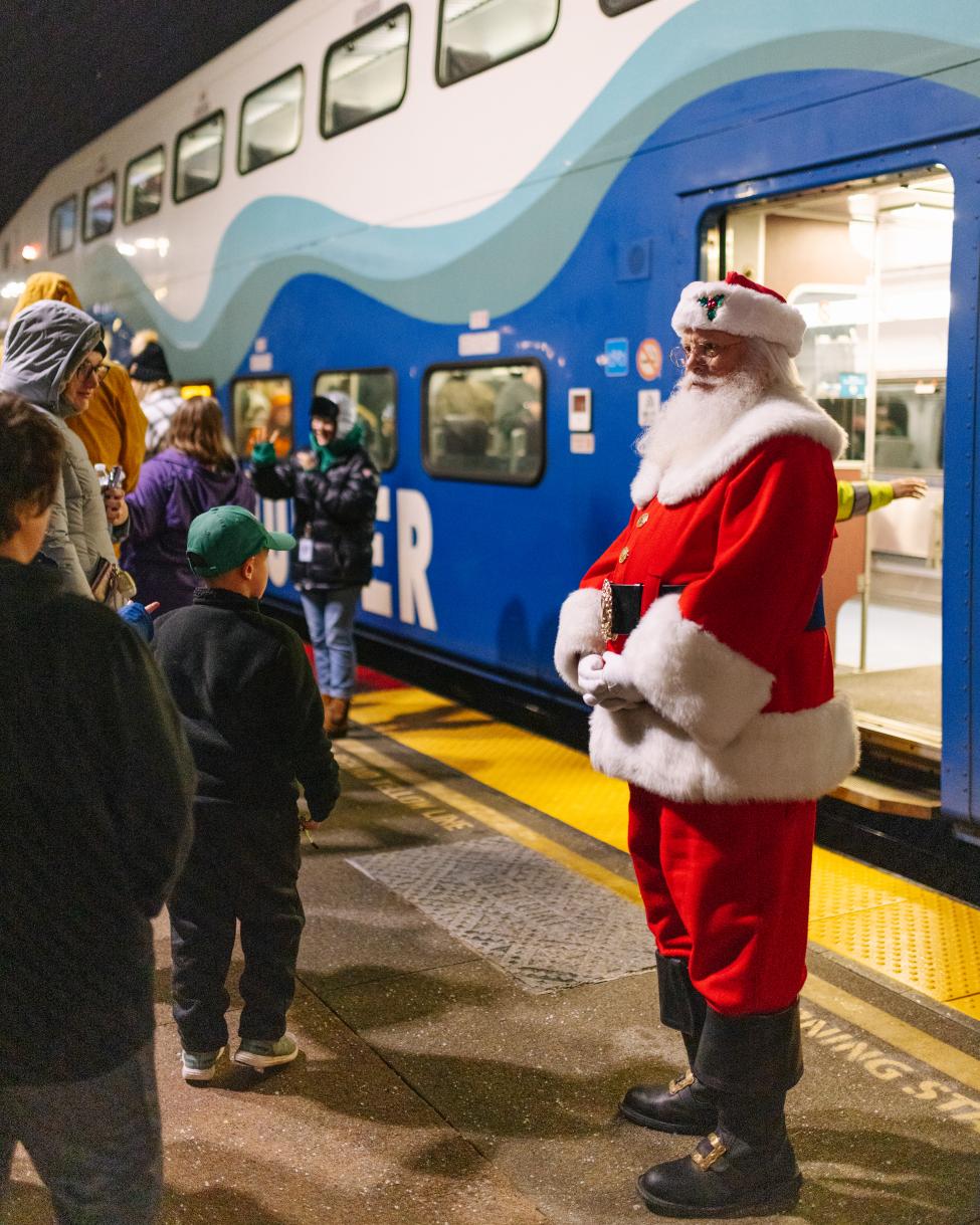 Santa stands on a Sounder platform talking to people, with a train in the background