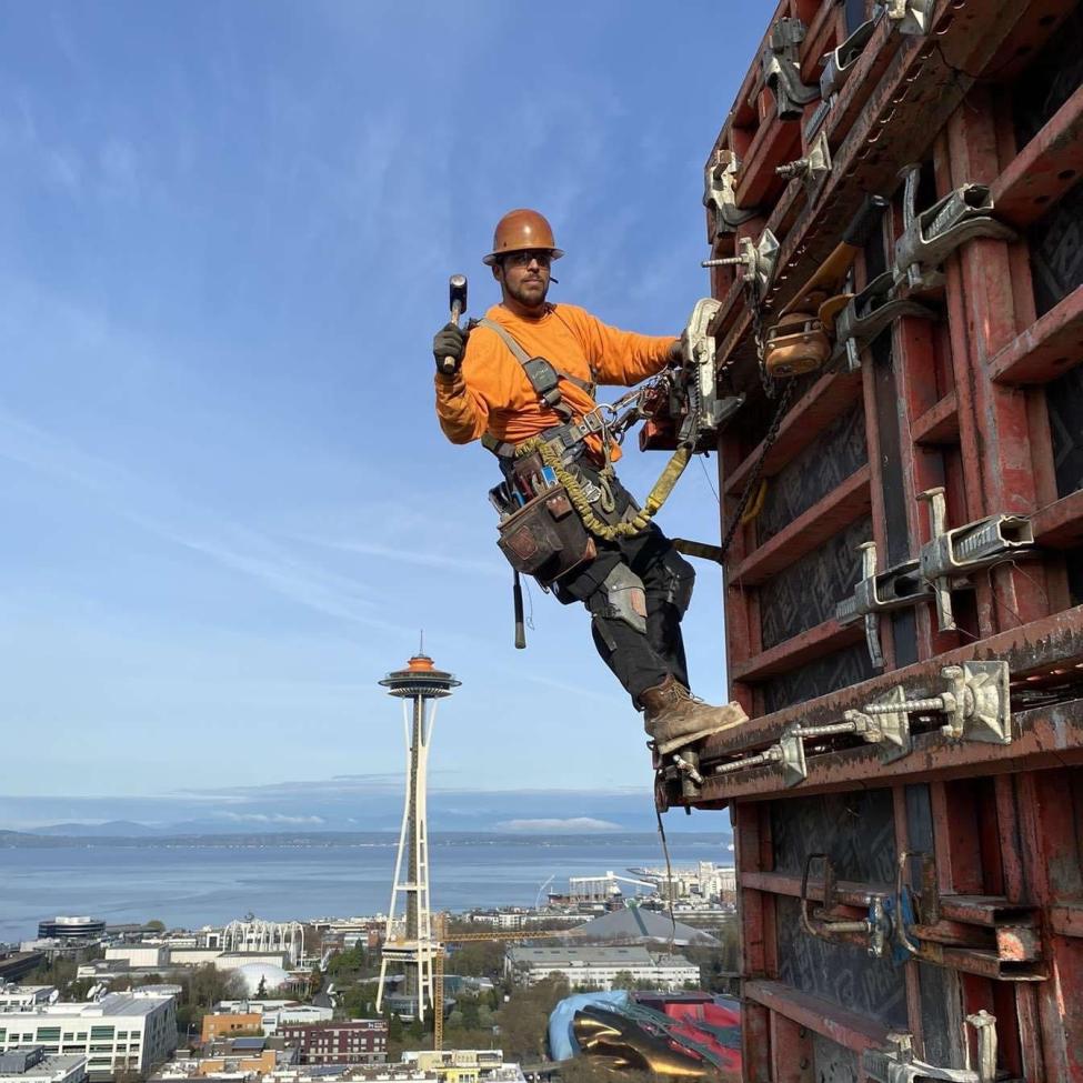 Wesley Holmes works on a tall building, with Seattle's Space Needle in the background