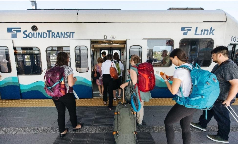 Passengers with luggage and backpacks wait to board a Link light rail train.