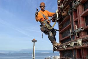 Wesley Holmes works on a tall building, with Seattle's Space Needle in the background