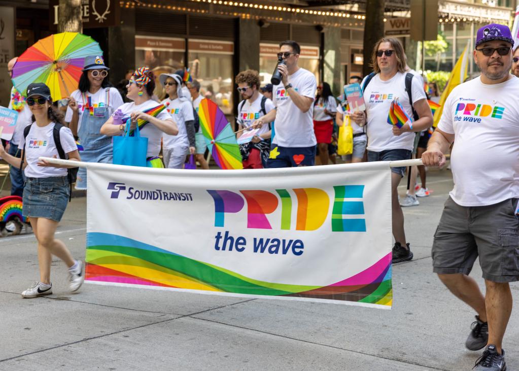 Sound Transit reps walk through the Pride parade holding a banner that reads, "Pride the Wave"