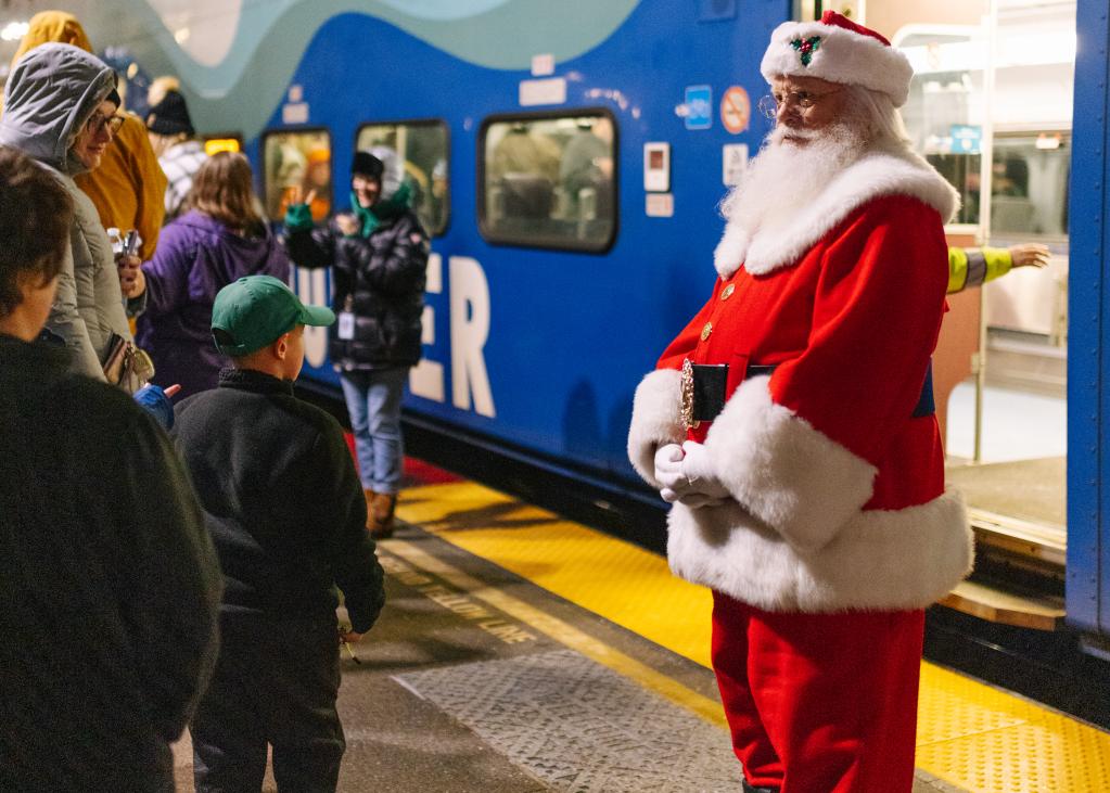 Santa stands on a Sounder platform talking to people, with a train in the background